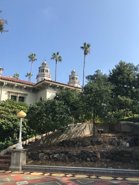 Spanish Colonial Revival mansion with ornate bell towers viewed from a manicured garden courtyard with palm trees. — Big Sur & the Highway 1 Coast