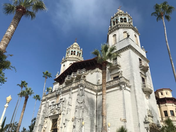Hearst Castle's white limestone facade and ornate towers framed by palm trees under clear sky, viewed from ground level. — Hearst Castle, Big Sur & the Highway 1 Coast