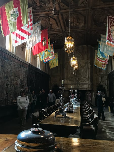 Interior of Hearst Castle's dining hall with ornate carved ceiling, hanging brass lanterns, heraldic banners, and a… — Hearst Castle, Big Sur & the Highway 1 Coast