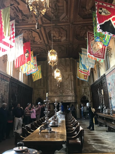 Interior of an ornate gothic dining hall with carved wooden ceiling, hanging brass lanterns, and heraldic banners at… — Big Sur & the Highway 1 Coast