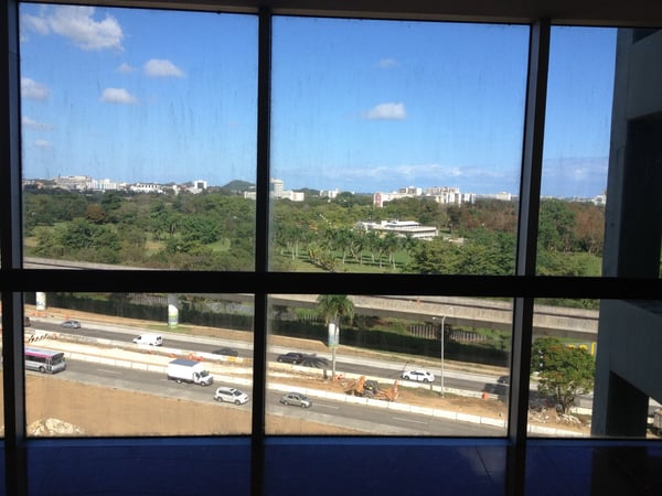Urban landscape with highway, residential areas, and palm trees viewed from an elevated indoor window in San Juan…