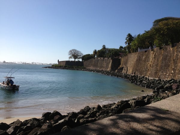 Historic stone fortification wall overlooking a turquoise beach cove with fishing boat, San Juan Antiguo. — Plazuela de Isabel I de Castilla, San Juan