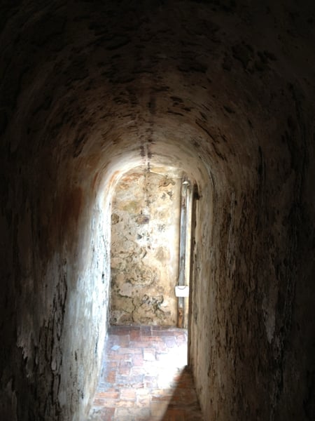 Ancient stone archway and vaulted corridor with deteriorating walls and brick flooring, viewed from within a… — San Juan