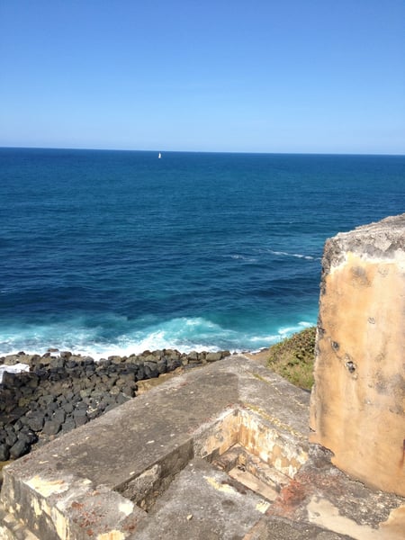 Coastal fortification ruins at Faro del Castillo San Felipe del Morro overlooking the Atlantic Ocean with a sailboat on… — Faro del Castillo San Felipe del Morro, San Juan