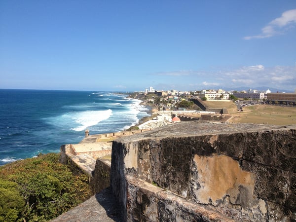 Historic fortification ruins overlooking a coastal beach with whitecap waves and colonial architecture visible on the… — Castillo San Felipe del Morro, San Juan