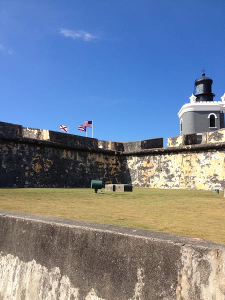 Fort San Felipe del Morro's courtyard with lighthouse and weathered stone walls under clear blue sky. — Faro del Castillo San Felipe del Morro, San Juan