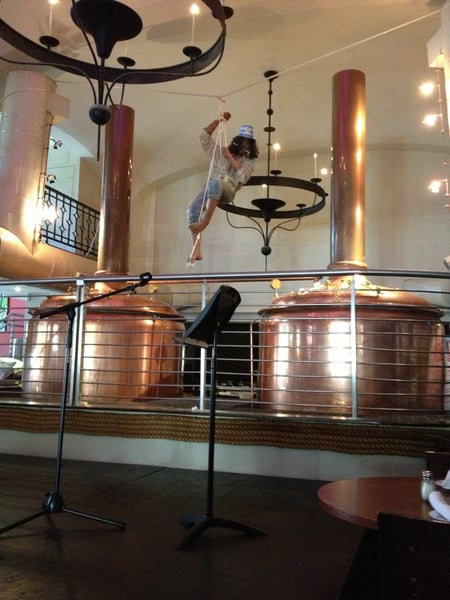 A person performing an aerial acrobatic stunt suspended from decorative metalwork installations in an indoor venue with… — Viejo San Juan, San Juan