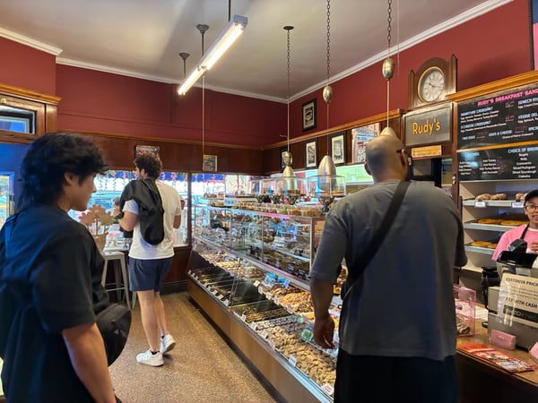 Interior of Rudy's Bakery in New York showing display cases with baked goods and customers at the counter. — New York City