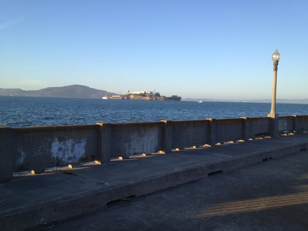 View from a waterfront pier toward a fortified island prison across the bay, with hills in the background under clear… — Fort Mason, San Francisco