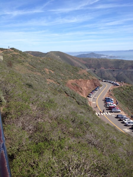 Parking area and winding coastal road viewed from hillside overlook at Marin Headlands, with bay waters visible in the… — San Francisco