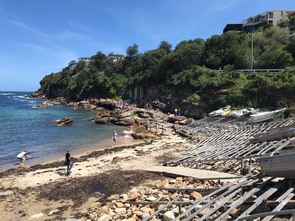 Rocky beach at Gordon's Bay with swimmers and boats on sand, rocky cove, and vegetation-covered cliffs in background. — Sydney