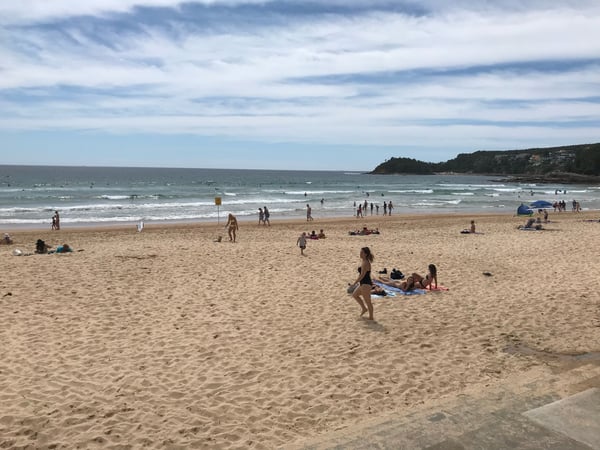 Manly Beach on a summer day with swimmers and beachgoers scattered across the sand and in the water, photographed from… — Sydney