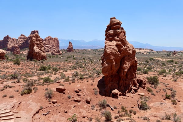 Distinctive red rock formations rise from the arid landscape of Castle Valley, Utah, with distant mountains visible on… — Arches National Park, Moab, Arches & Canyonlands