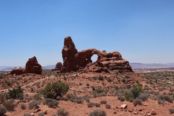 Distinctive red rock formations with natural arch in Castle Valley's arid desert landscape under clear sky. — Arches National Park, Moab, Arches & Canyonlands