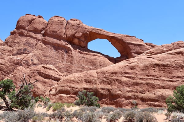 Skyline Arch, a natural rock arch formation in the Moab area, photographed from ground level against a clear blue sky. — Skyline Arch Trail, Moab, Arches & Canyonlands