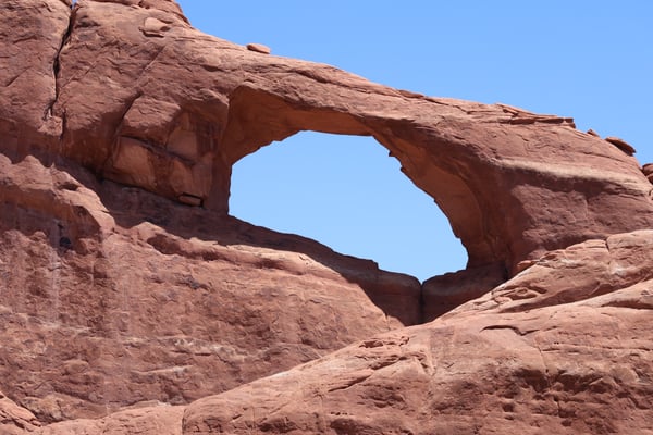 Natural stone arch formation in red sandstone desert landscape under clear blue sky, photographed from ground level. — Skyline Arch Trail, Moab, Arches & Canyonlands