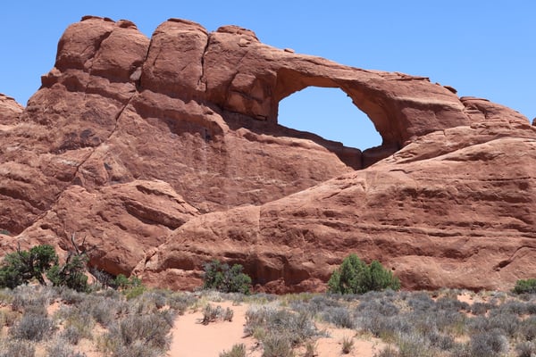 Arch formation with natural opening in red sandstone rock face in a desert landscape with sparse vegetation. — Skyline Arch Trail, Moab, Arches & Canyonlands