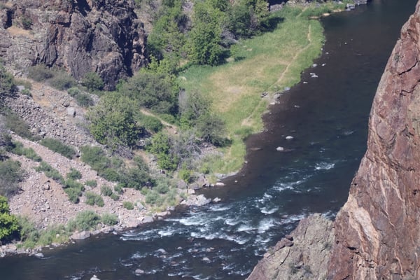 Painted Wall View overlooks a rocky river canyon with steep red cliffs, flowing water, and forested slopes in Crawford… — Painted Wall View, Black Canyon of the Gunnison