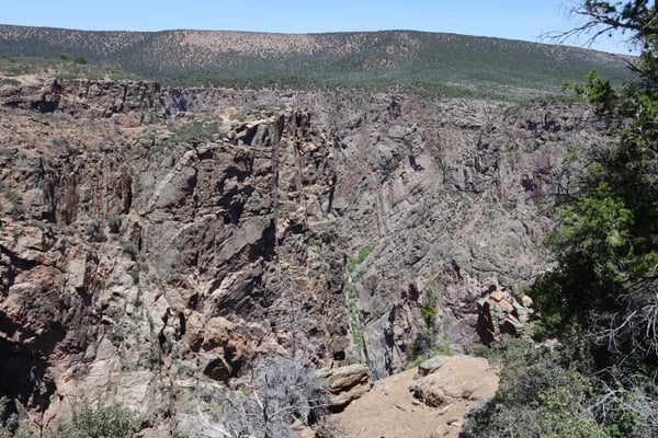 Deep rocky canyon with columnar basalt formations viewed from a hiking trail, with forested ridges visible in the… — Rock Point, Black Canyon of the Gunnison