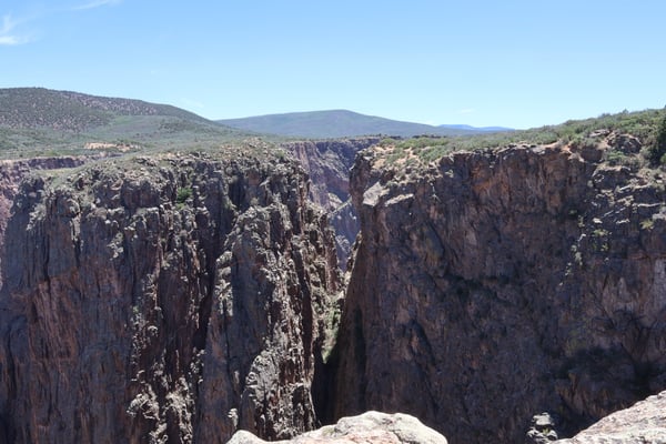 Deep columnar basalt canyon at Rock Point viewed from an overlook, with rolling desert hills beyond. — Rock Point, Black Canyon of the Gunnison