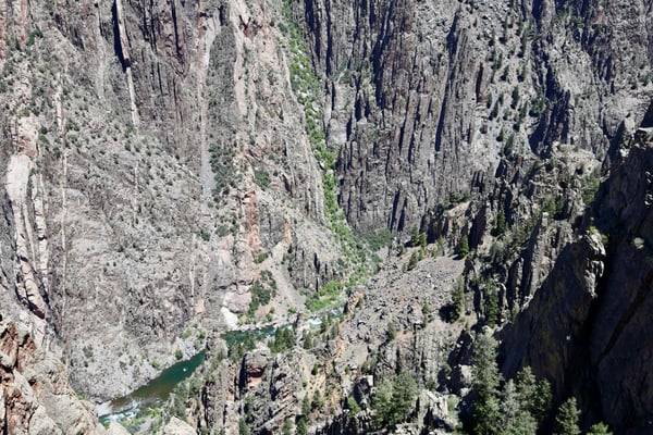 Deep canyon with columnar rock formations and a river visible at the base, viewed from Gunnison Point overlook. — Black Canyon of the Gunnison