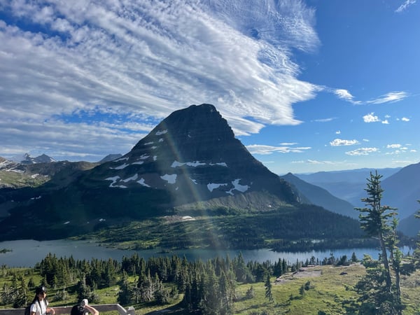 Mountain peak with patches of snow overlooking a forested valley and alpine lake, viewed from Hidden Lake Overlook. — Glacier National Park