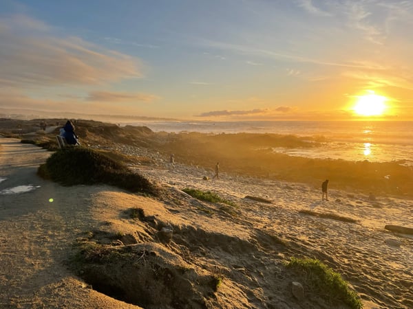Sunset over the Pacific Ocean from rocky coastal bluffs in Pacific Grove, with beachgoers on the sand below. — Big Sur & the Highway 1 Coast