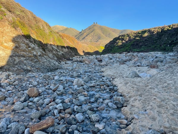 Rocky riverbed with sandy banks framed by arid hillsides under clear blue sky. — Big Sur & the Highway 1 Coast
