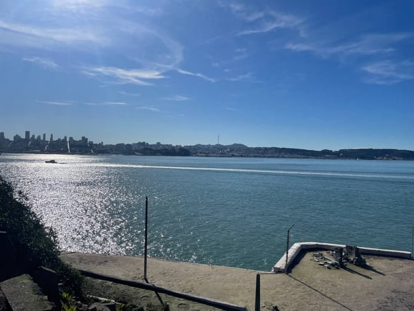 San Francisco skyline viewed across the bay from a sandy beach with wooden pier structures in the foreground. — Alcatraz Island, San Francisco