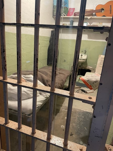 Historic prison cell at Alcatraz Island viewed through barred gate, showing sparse furnishings and green-painted walls. — Alcatraz Island, San Francisco