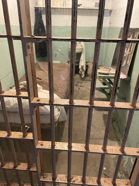 Prison cell interior at Alcatraz Island with metal bars and sparse furnishings visible through the cell door. — Alcatraz Island, San Francisco