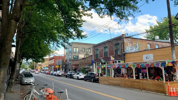 Historic brick buildings line a tree-shaded street in Portland's Belmont neighborhood, featuring shops with colorful… — Laurelhurst, Portland
