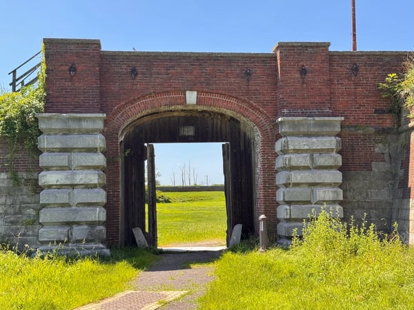 Historic red brick gateway with arched entrance framing pastoral farmland beyond, likely a Civil War-era fortification… — Southwest Philadelphia, Philadelphia