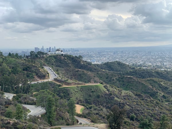 Los Angeles skyline viewed from Griffith Park hilltop, with winding roads through chaparral-covered hills in the… — Griffith Park, Los Angeles