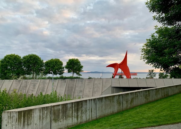 Red abstract sculpture at Olympic Sculpture Park with Puget Sound and mountains visible beyond concrete walls. — Olympic Sculpture Park, Seattle