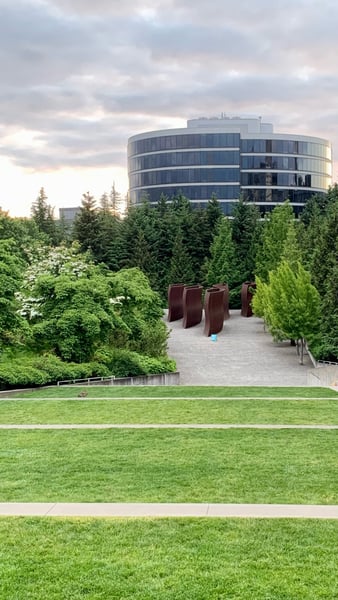 Modern circular building with curved glass facade viewed from a manicured park with coniferous trees and abstract metal… — Belltown, Seattle