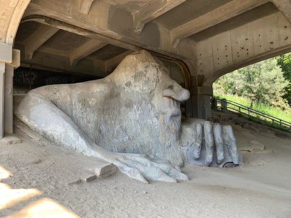 Large stone sculpture of a reclining figure sheltered beneath a concrete bridge overpass in Fremont, Seattle.