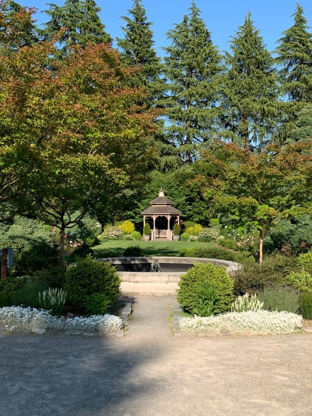 A manicured garden with a gazebo, pond, and mature trees viewed along a gravel pathway in a Seattle park. — Phinney Ridge, Seattle