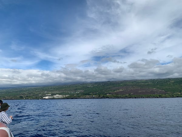 Coastal view of Kona, Hawaii from a boat, showing lush green volcanic landscape and white resort buildings along the… — Big Island, Hawaii