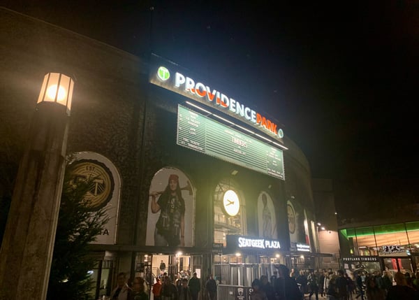 Providence Park illuminated at night with marquee signage and crowds gathered outside the venue in Portland. — Goose Hollow, Portland