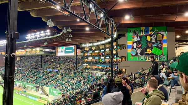 Packed soccer stadium at night with crowds in stands and 'Stand Together' banner visible at Portland venue. — Goose Hollow, Portland