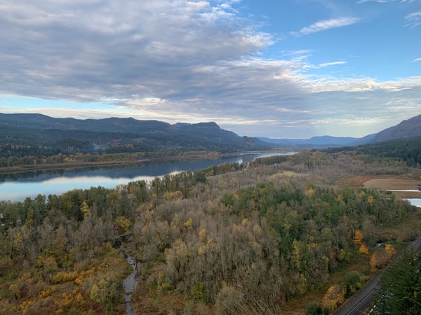 Aerial view of a river valley with forested banks, mountains in the distance, and autumn foliage under partly cloudy… — Mount Hood National Forest, Columbia River Gorge