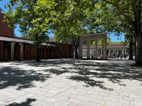 Historic plaza with brick buildings and classical colonnade structures shaded by mature trees, Ankeny Plaza. — Old Town, Portland