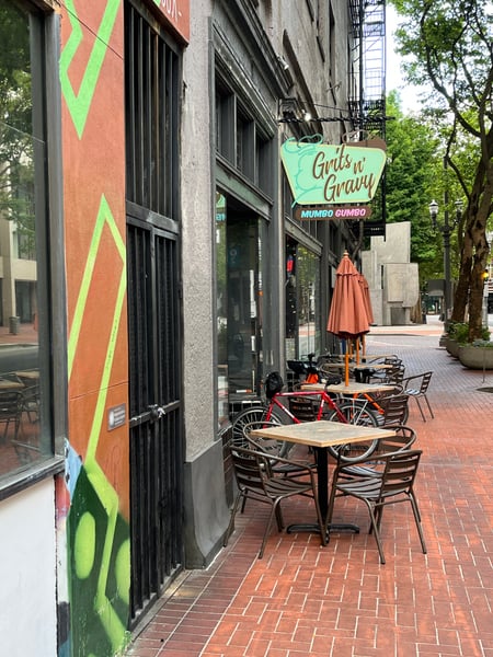 Outdoor seating at Grits n Gravy restaurant on a brick pedestrian street with colorful street art and bicycles parked… — Downtown, Portland