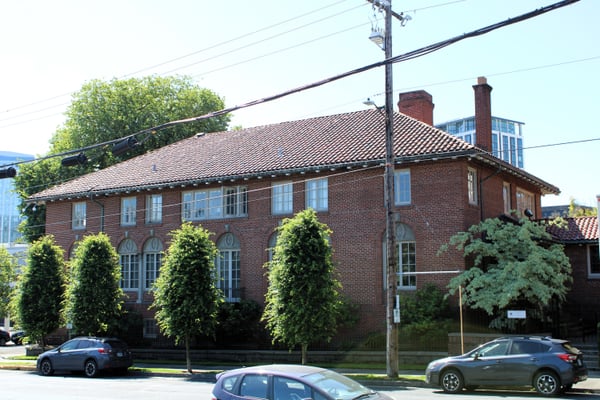 Red brick Romanesque Revival building with decorative chimneys and ivy-covered facade, viewed from street level with… — Goose Hollow, Portland