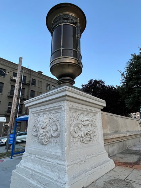 Ornamental stone pedestal with decorative urn-shaped lamp fixture, a public monument in an urban setting. — Goose Hollow, Portland
