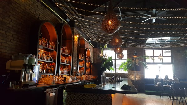 Interior of an upscale bar with illuminated bottle displays, decorative pendant lights, and patrons seated by large… — Pearl District, Portland