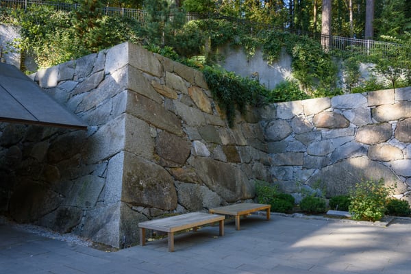 Stone retaining wall with wooden benches in a landscaped garden courtyard surrounded by mature trees. — Portland Japanese Garden, Portland