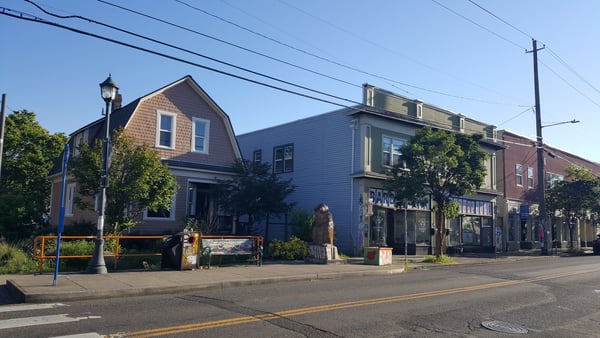 Historic street corner in Northeast Portland with mixed-use buildings, storefronts, and residential architecture under…