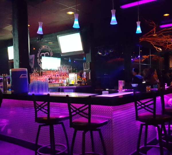 Interior of a nightclub bar with neon purple lighting, illuminated pendant fixtures, and a fully stocked bar counter. — Old Town, Portland